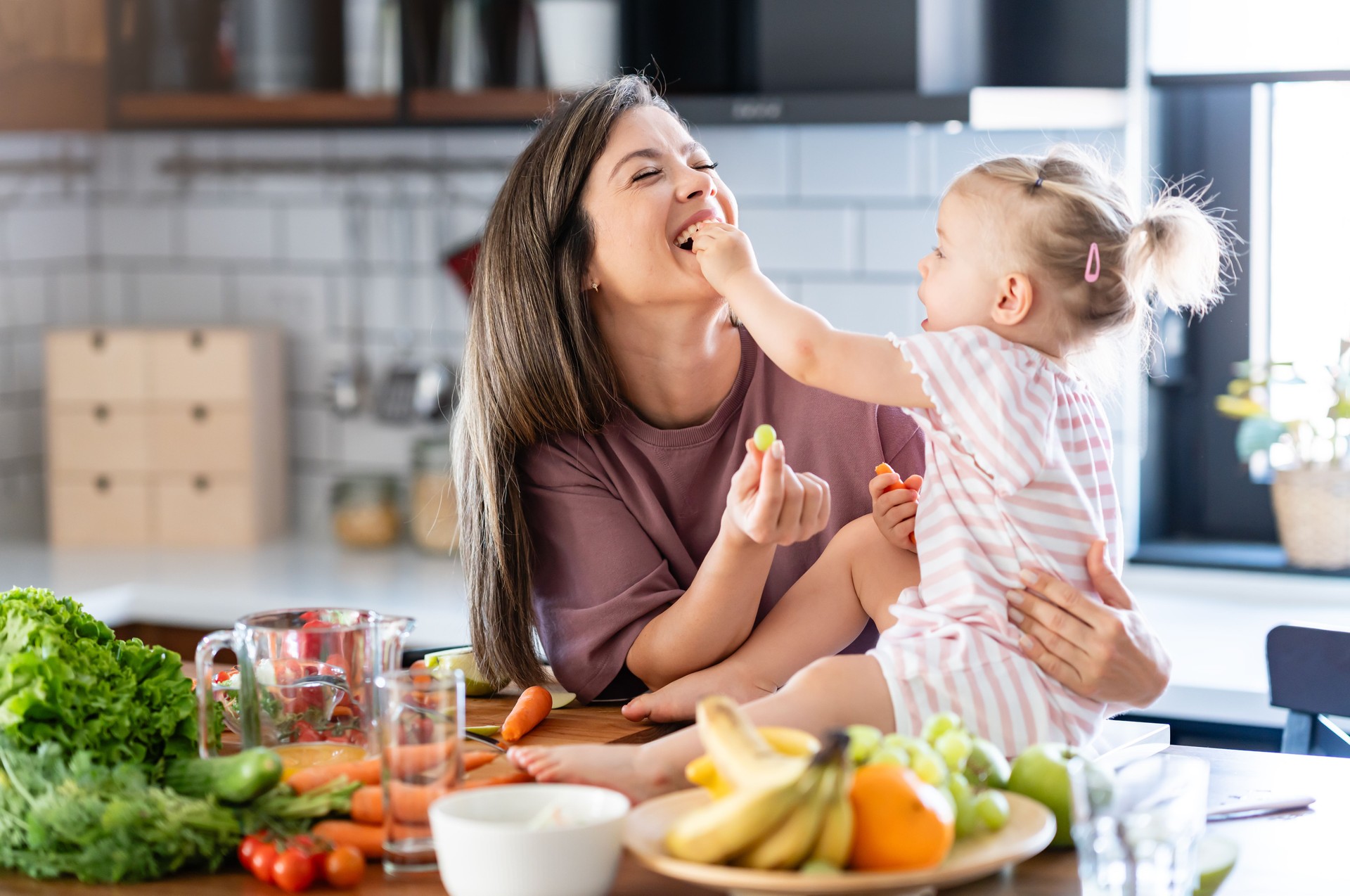 The mother prepared a healthy fruit and yogurt meal rich in vitamins, and she's feeding her cute little baby daughter at the home kitchen counter